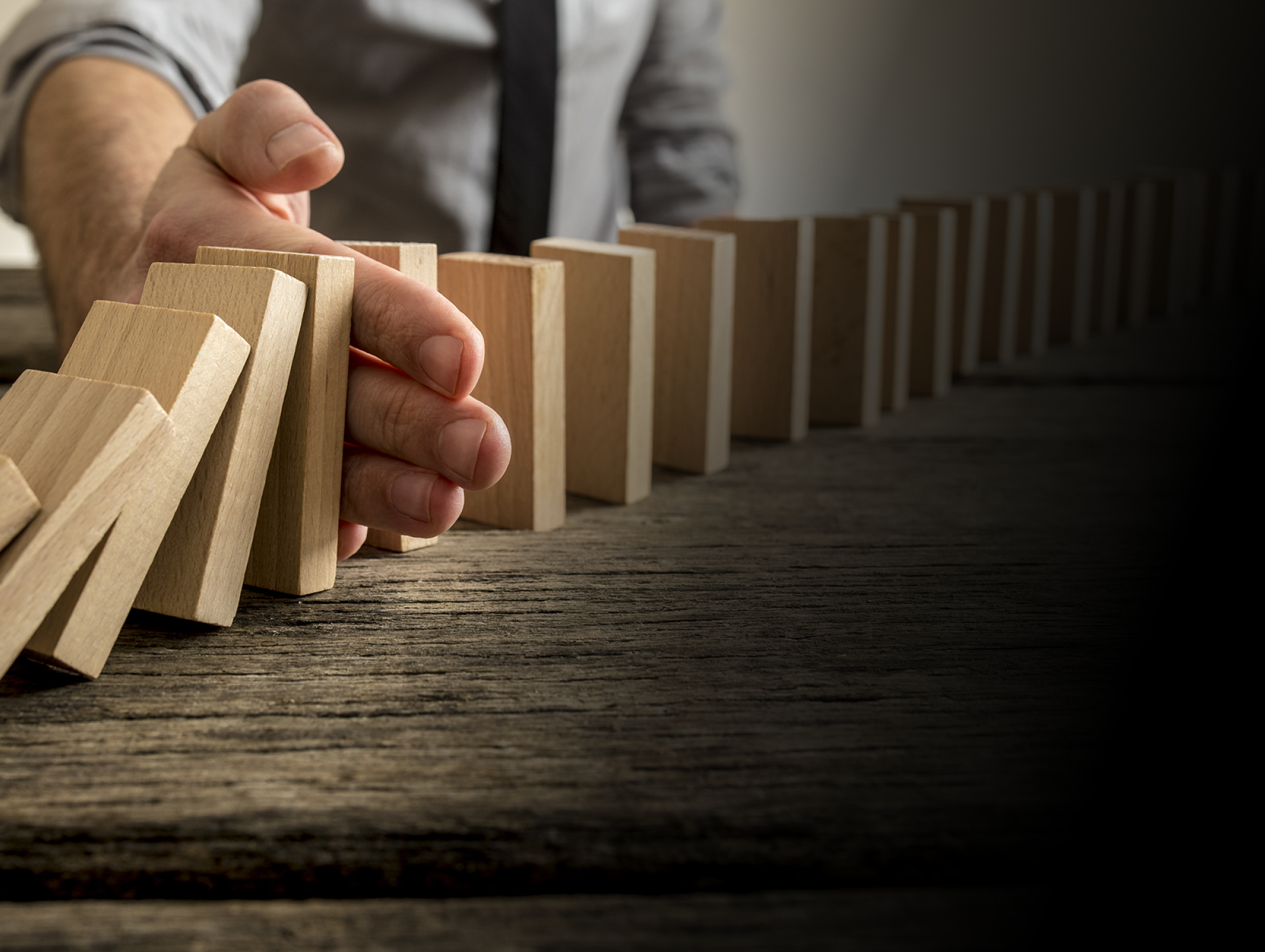 Man stopping domino effect on wooden table  Business success concept  Copy space 