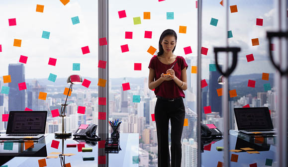 Mixed race secretary working in modern office in skyscraper  writing and sticking adhesive notes with tasks on window  