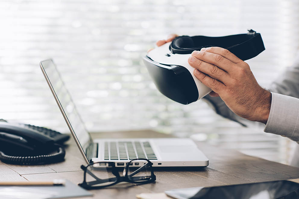 Corporate businessman working at office desk and holding a virtual reality headset: business and innovative technology concept